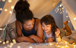 Two girls laying in a tent look at a tablet