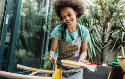 Smiling woman painting a chair outside with yellow color